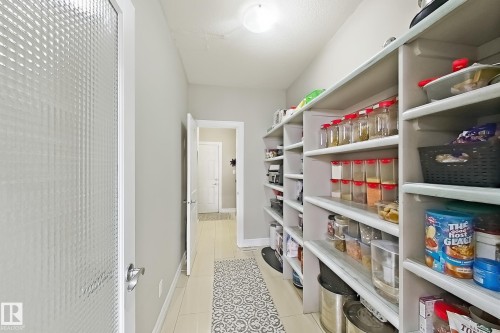 Walk-in pantry featuring built-in shelving, tile flooring, and a textured glass door - 144 52 Street Sw, Edmonton, AB 
