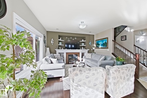 Spacious living area featuring a fireplace with a white mantel, dark wood-finish flooring, a prominent staircase with dark wood railings, and recessed ceiling lighting - 144 52 Street Sw, Edmonton, AB 