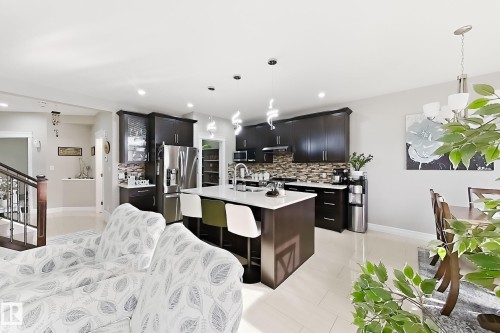 Open-concept living space featuring a kitchen island with seating, dark wood cabinetry, and stainless steel appliances - 144 52 Street Sw, Edmonton, AB 