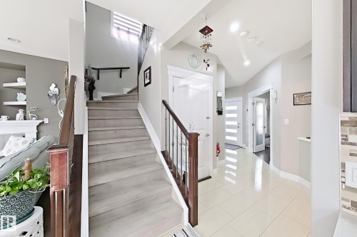 Grand entryway featuring a staircase with wood-finish treads and railing, ceramic tile flooring, and recessed lighting - 144 52 Street Sw, Edmonton, AB 