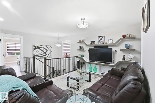 Open-concept living space featuring a custom built-in media center with shelving, contemporary light fixtures, and iron railings - 144 52 Street Sw, Edmonton, AB 