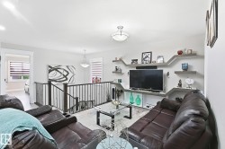 Open-concept living space featuring a custom built-in media center with shelving, contemporary light fixtures, and iron railings - 