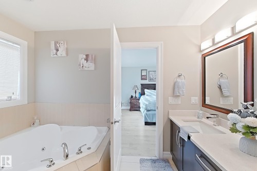 Jetted corner tub with tiled surround, dual vanity with undermount sinks, framed mirror, and chrome fixtures - 144 52 Street Sw, Edmonton, AB 