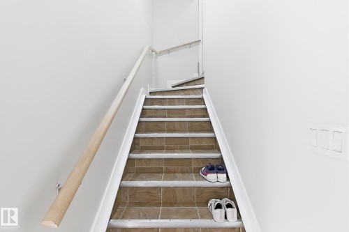 Staircase with tile steps, white risers, and a natural wood handrail - 144 52 Street Sw, Edmonton, AB 
