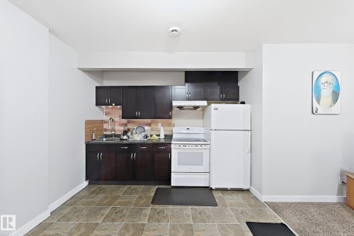 Kitchen featuring dark wood-finish cabinetry, white appliances, and a wood-look tile backsplash - 144 52 Street Sw, Edmonton, AB 