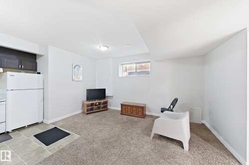White refrigerator with top freezer, dark wood-finish cabinetry, tile flooring, and light carpeting - 144 52 Street Sw, Edmonton, AB 