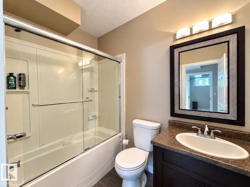 Bathroom featuring a dark wood-finish vanity, an oval undermount sink, a dark countertop, and a framed mirror with overhead lighting - 144 52 Street Sw, Edmonton, AB 