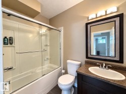 Bathroom featuring a dark wood-finish vanity, an oval undermount sink, a dark countertop, and a framed mirror with overhead lighting - 