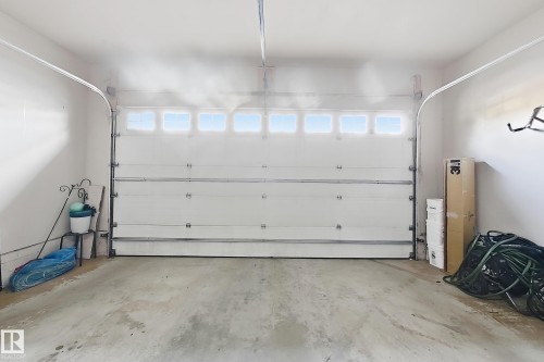 Attached garage with a white panel door and upper window lights, featuring a concrete floor and painted walls - 144 52 Street Sw, Edmonton, AB 