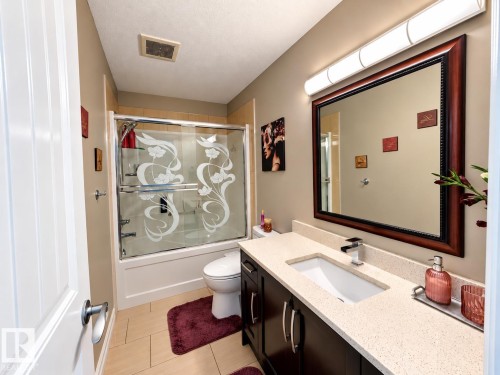 Recessed lighting, wood-finish vanity with a rectangular undermount sink, stone-finish countertop, and a framed mirror - 144 52 Street Sw, Edmonton, AB 