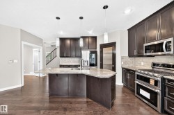 Kitchen featuring a central island with an undermount sink, pendant lighting, stainless steel appliances, dark wood cabinetry, and wood-finish flooring - 
