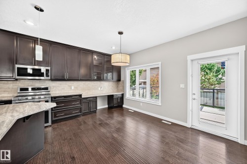 Dark wood-finish flooring, rich cabinetry, light-toned countertops, stainless steel appliances, and a glass-paneled exterior door - 3329 West Court Nw, Edmonton, AB 