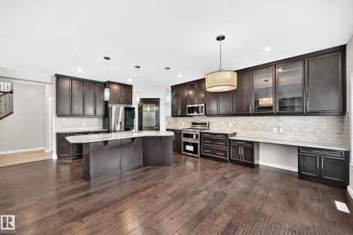Spacious kitchen featuring dark wood-finish cabinetry, a large center island, stainless steel appliances, and wood-finish flooring - 3329 West Court Nw, Edmonton, AB 