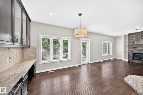 Hardwood-finish flooring throughout, integrated stone-clad fireplace, built-in shelving, white trim, and a glass-paneled exterior door - 3329 West Court Nw, Edmonton, AB 