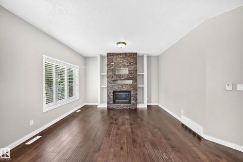 Stone-clad fireplace with built-in shelving, wood-finish flooring, and a large window with blinds - 3329 West Court Nw, Edmonton, AB 