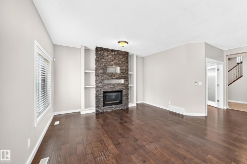 Stacked stone fireplace with an integrated firebox, flanked by built-in shelving and dark wood-finish flooring - 3329 West Court Nw, Edmonton, AB 