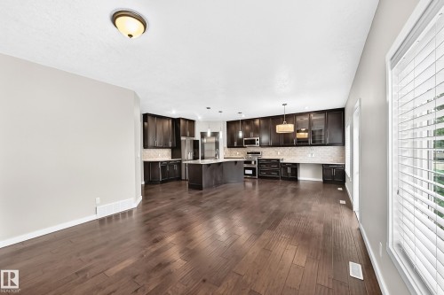 Spacious open-concept interior featuring wood-finish flooring, dark wood cabinetry, a central island, and stainless-steel appliances - 3329 West Court Nw, Edmonton, AB 