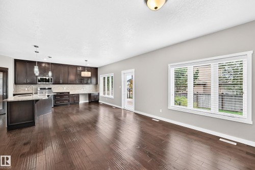Open-concept room featuring wood-finish flooring, dark wood cabinetry, a large kitchen island, and a glass-paned door - 3329 West Court Nw, Edmonton, AB 
