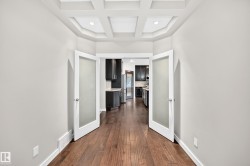 Coffered ceiling with recessed lighting, wood-finish flooring, and double doors with frosted glass panels - 
