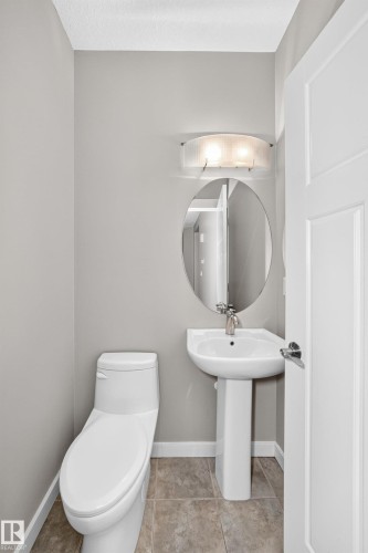 Pedestal sink with chrome faucet, oval wall mirror, and modern wall-mounted light fixture - 3329 West Court Nw, Edmonton, AB 