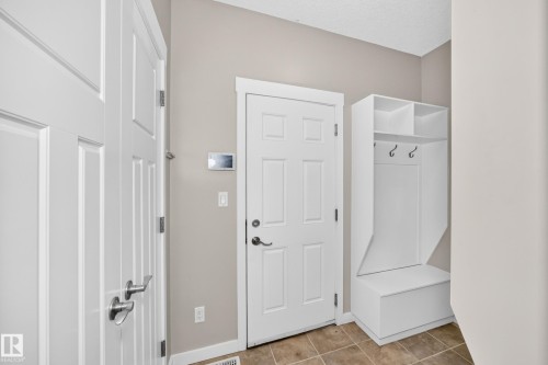 Entry area featuring tile flooring, white paneled doors, and a built-in storage bench with shelving and coat hooks - 3329 West Court Nw, Edmonton, AB 