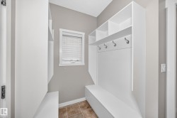Built-in shelving unit with coat hooks and bench seating, complete with a window featuring blinds and tile flooring - 