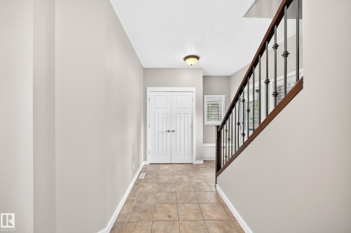 Neutral wall paint, tile flooring, white double doors, staircase with dark wood handrail, and black wrought iron balusters - 3329 West Court Nw, Edmonton, AB 