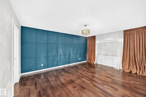 Wood-finish flooring, accent wall with decorative paneling, window with blinds, and an ornate ceiling light fixture - 3329 West Court Nw, Edmonton, AB 