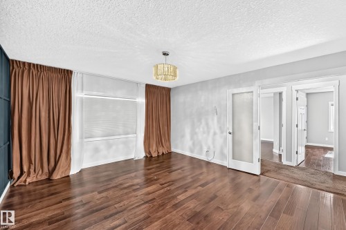 Wood-finish flooring, a contemporary chandelier, textured ceiling, a window with blinds, and white doors with frosted glass panels - 3329 West Court Nw, Edmonton, AB 