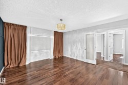 Wood-finish flooring, a contemporary chandelier, textured ceiling, a window with blinds, and white doors with frosted glass panels - 
