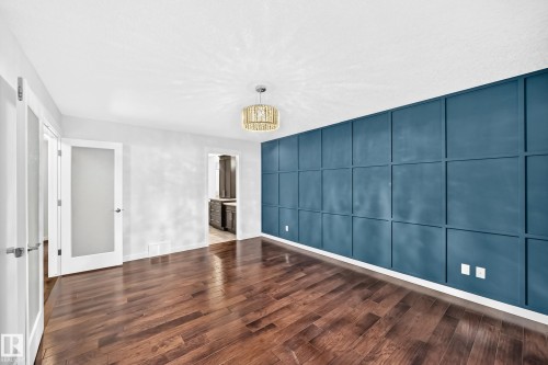 Wood-finish flooring, accent wall with panel molding, contemporary chandelier, white interior doors with frosted glass, and white trim - 3329 West Court Nw, Edmonton, AB 
