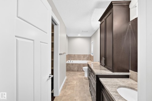 Dual vanity with stone countertop, dark wood-finish cabinetry, built-in soaking tub, and tile flooring - 3329 West Court Nw, Edmonton, AB 