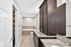 Bathroom featuring a built-in tub with tile surround, tile flooring, dark wood-finish cabinetry, light-toned stone countertops, and a recessed storage area with shelving - 