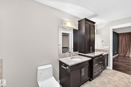 Dual vanity with granite countertops, dark wood cabinetry, integrated sink, and tiled flooring - 3329 West Court Nw, Edmonton, AB 