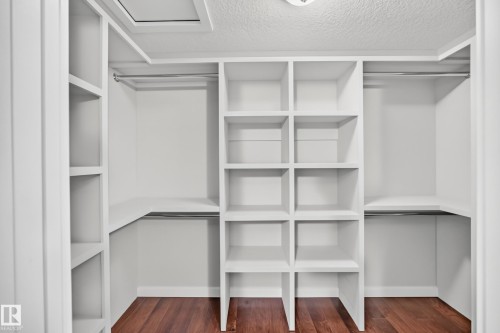 Custom built-in closet system featuring multiple shelves, hanging rods, and wood-finish flooring - 3329 West Court Nw, Edmonton, AB 