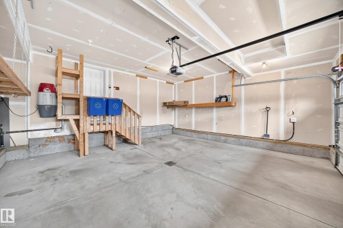 Spacious garage with concrete flooring, built-in wooden shelving, and overhead door mechanism - 3329 West Court Nw, Edmonton, AB 