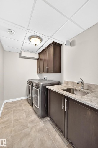 Laundry area featuring square tile flooring, dark wood-finish cabinetry, a built-in stainless steel sink, and a light-toned countertop - 3329 West Court Nw, Edmonton, AB 