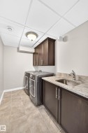 Laundry area featuring square tile flooring, dark wood-finish cabinetry, a built-in stainless steel sink, and a light-toned countertop - 