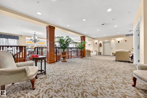 Spacious common area featuring patterned carpet, recessed lighting, architectural columns, and a visible elevator - #420 9820 165 St Nw, Edmonton, AB 