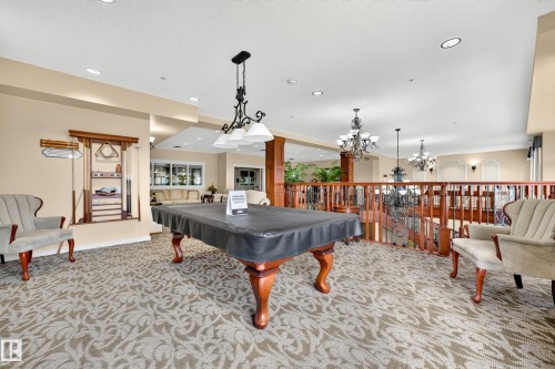 Spacious entertainment area featuring decorative carpet, a billiard table with a dedicated overhead light fixture, and a built-in cue rack - #420 9820 165 St Nw, Edmonton, AB 