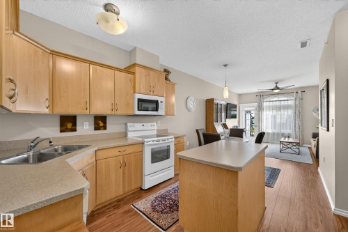 Kitchen featuring light wood-finish cabinetry, a built-in microwave, and a double basin sink - #420 9820 165 St Nw, Edmonton, AB 