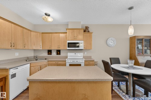 Kitchen featuring wood-finish cabinetry, a central island with countertop, and white appliances - #420 9820 165 St Nw, Edmonton, AB 