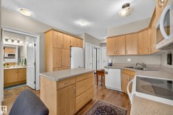 Kitchen featuring wood-finish flooring, light wood cabinetry, white appliances, a center island with countertop, and overhead lighting fixtures - 