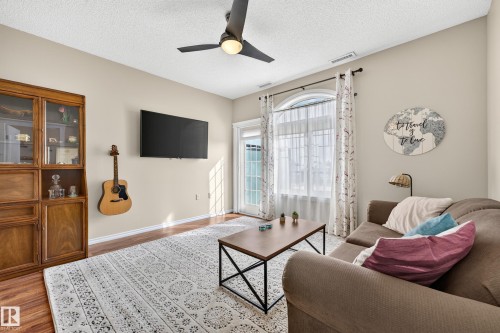 Wood-finish flooring, ceiling fan with integrated lighting, built-in display cabinetry, and an arched transom window above the patio door - #420 9820 165 St Nw, Edmonton, AB 