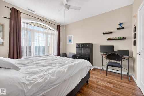 Arched window with gridded panes, ceiling fan, wood-finish flooring, and light-toned walls - #420 9820 165 St Nw, Edmonton, AB 