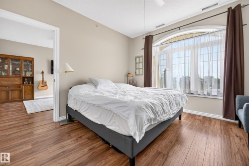 Wood-finish flooring throughout, arched window with transom, ceiling fan, and neutral wall tones - #420 9820 165 St Nw, Edmonton, AB 