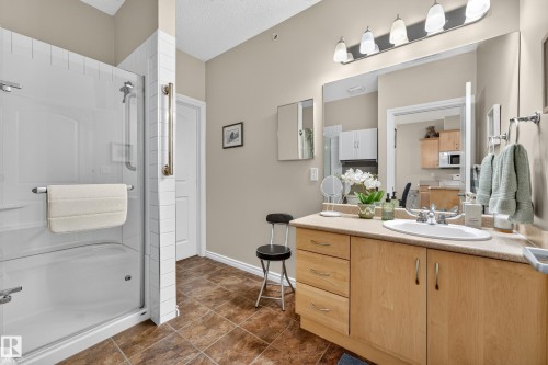 Bathroom featuring a bathtub with an integrated shower, a wood-finish vanity with an integrated sink, and an expansive wall mirror - #420 9820 165 St Nw, Edmonton, AB 