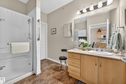 Bathroom featuring a bathtub with an integrated shower, a wood-finish vanity with an integrated sink, and an expansive wall mirror - 
