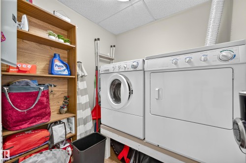Dedicated laundry area featuring white appliances and wood-finish shelving - #420 9820 165 St Nw, Edmonton, AB 