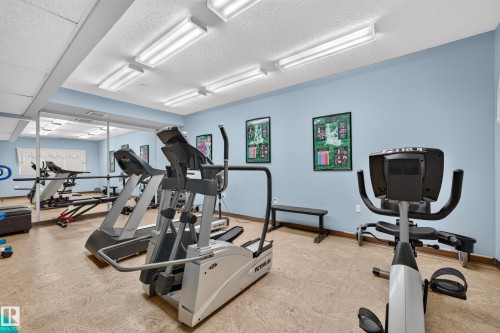 Dedicated fitness room featuring a full wall mirror, recessed fluorescent lighting, and durable flooring - #420 9820 165 St Nw, Edmonton, AB 